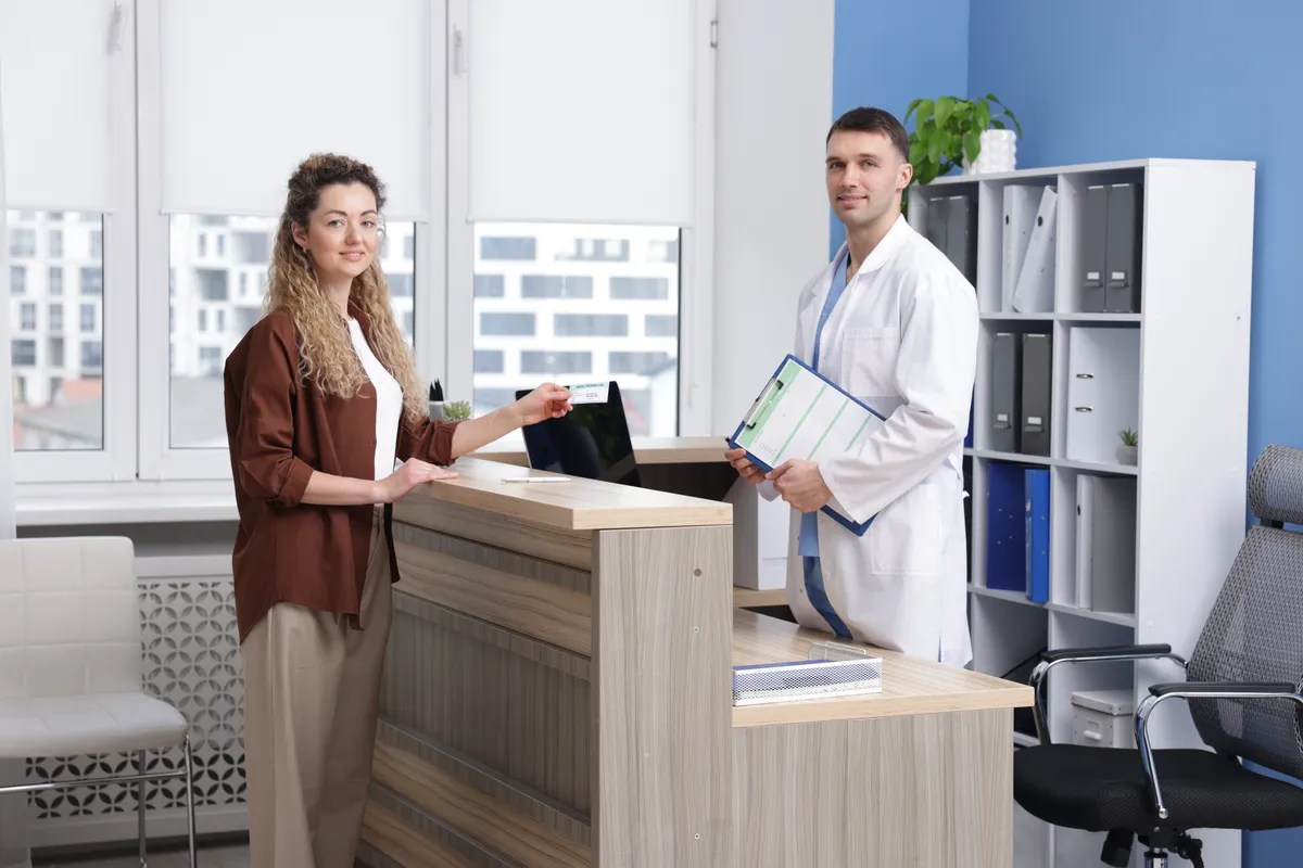 Patient handing medical insurance card to receptionist for HIPAA-compliant payment processing